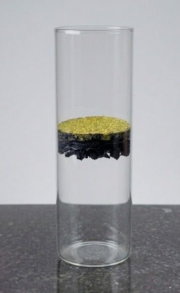 Amostra real do piso drenante em corte: camada colorida sobre o colchão de raspa de borracha